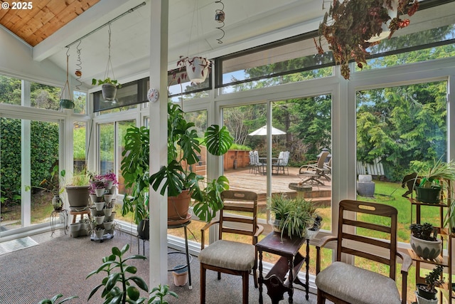 sunroom with beamed ceiling, wooden ceiling, outdoor dining space, a wooden deck, and high vaulted ceiling