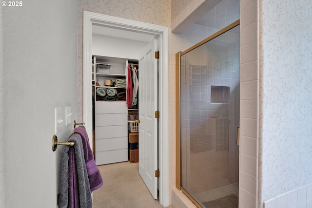 bathroom with a shower stall, a walk in closet, and wallpapered walls