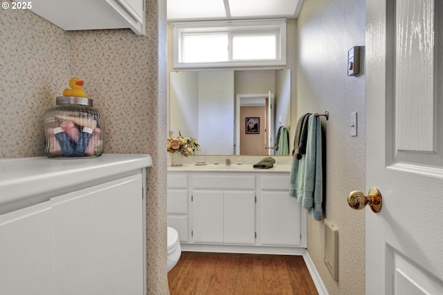 bathroom with wallpapered walls, wood finished floors, vanity, and toilet