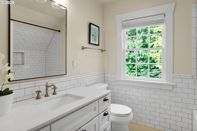 bathroom with tile walls, toilet, vanity, and a tile shower