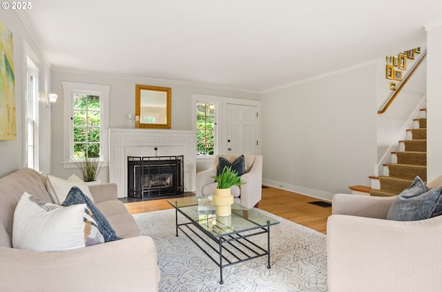 living room featuring a healthy amount of sunlight, light hardwood / wood-style flooring, crown molding, and a fireplace