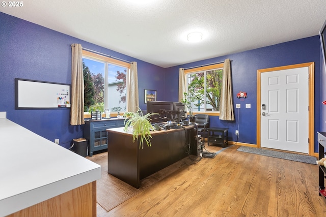office area featuring light wood finished floors, baseboards, and a textured ceiling
