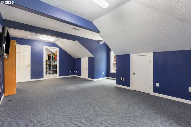 additional living space featuring a textured ceiling, vaulted ceiling, baseboards, and carpet flooring