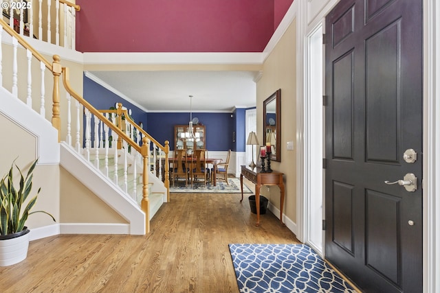 foyer entrance featuring stairs, crown molding, wood finished floors, a chandelier, and baseboards