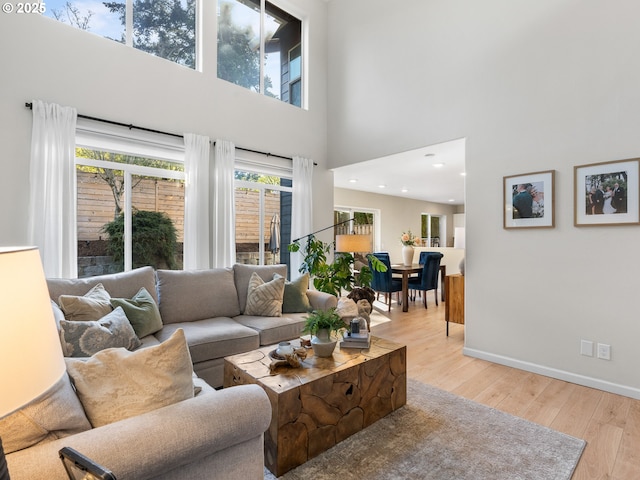 living area featuring recessed lighting, baseboards, light wood-type flooring, and a towering ceiling