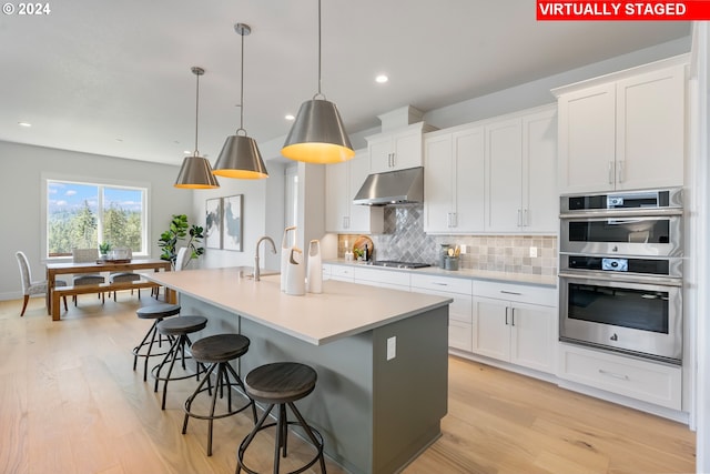 kitchen featuring white cabinetry, hanging light fixtures, a kitchen island with sink, and appliances with stainless steel finishes