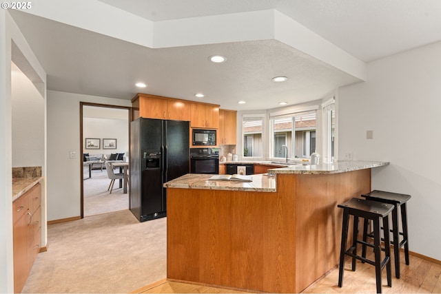 kitchen featuring a peninsula, baseboards, light stone counters, and black appliances