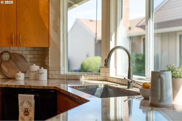 kitchen featuring light stone counters, a sink, dishwasher, brown cabinetry, and decorative backsplash