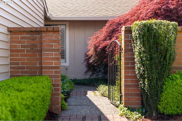 entrance to property with brick siding, a gate, and roof with shingles
