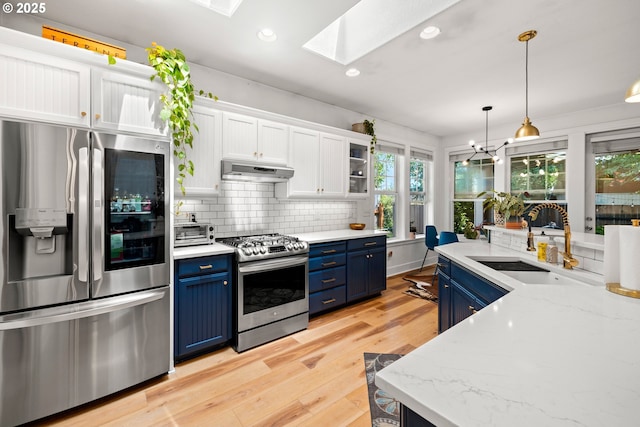 9628 N Exeter Ave, Portland, OR 97203 - kitchen with appliances with stainless steel finishes, blue cabinets, under cabinet range hood, white cabinetry, and a skylight
