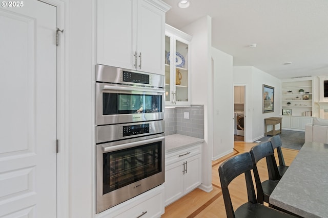 10440 SW 141st Ave, Beaverton, OR 97008 - kitchen with stainless steel double oven, washer / dryer, open floor plan, glass insert cabinets, and white cabinetry