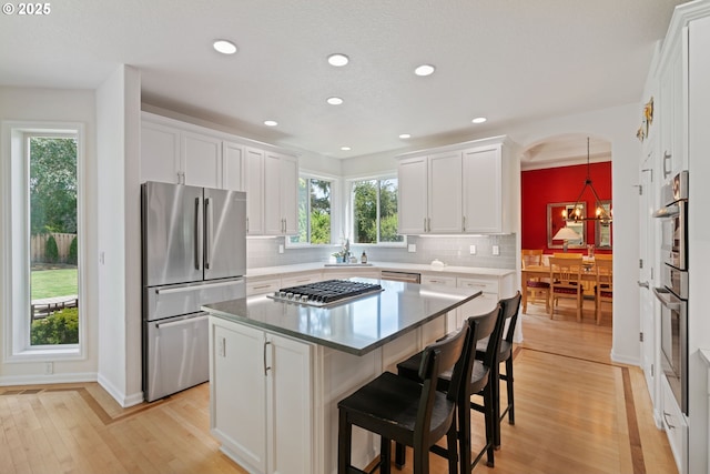10440 SW 141st Ave, Beaverton, OR 97008 - kitchen with stainless steel appliances, light wood-style flooring, backsplash, white cabinetry, and a kitchen bar