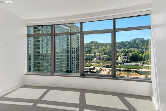 carpeted empty room with a view of city and baseboards