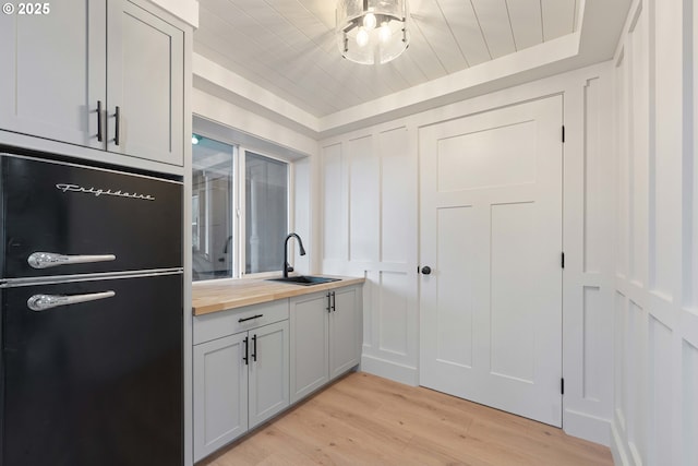 kitchen with light hardwood / wood-style flooring, butcher block countertops, black fridge, and sink