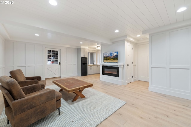 living room with light hardwood / wood-style flooring, wood ceiling, and sink