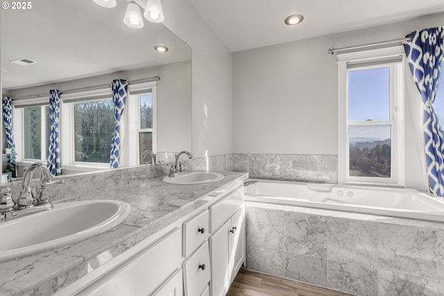 bathroom featuring hardwood / wood-style flooring, tiled tub, and vanity