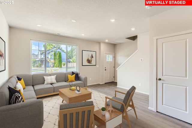 living area featuring recessed lighting, baseboards, light wood-style floors, and a textured ceiling