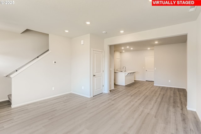 unfurnished living room with stairway, recessed lighting, light wood-type flooring, and a sink