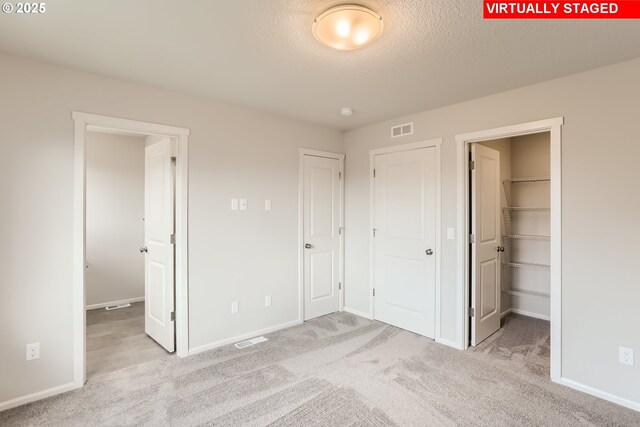 unfurnished bedroom featuring a walk in closet, visible vents, a closet, carpet, and baseboards