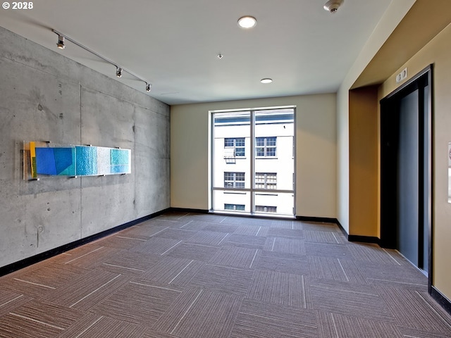 unfurnished room with elevator, carpet floors, rail lighting, and baseboards