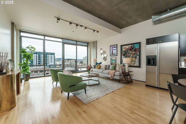 living room featuring rail lighting, light wood-type flooring, expansive windows, and a view of city