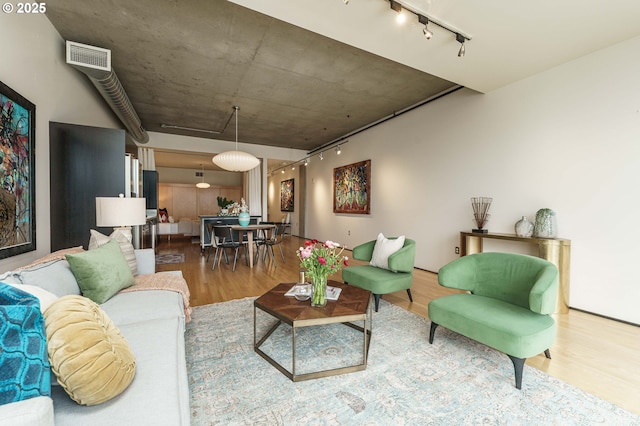 living area with rail lighting, wood finished floors, and attic access
