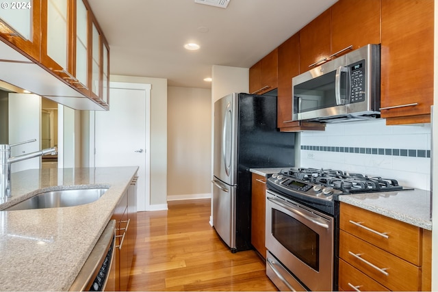 1500 SW 11th Ave Unit 1703, Portland, OR 97201 - kitchen featuring brown cabinets, light wood-style flooring, a sink, backsplash, and appliances with stainless steel finishes