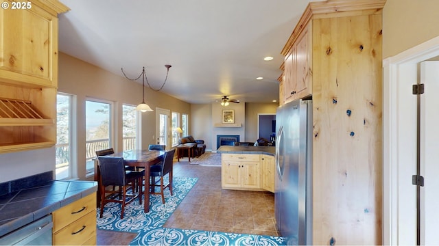 kitchen with tile countertops, light brown cabinetry, stainless steel appliances, a glass covered fireplace, and open floor plan