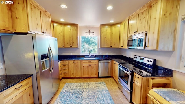 kitchen with light brown cabinetry, dark stone countertops, recessed lighting, stainless steel appliances, and a sink