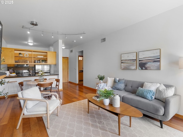 living area with rail lighting, visible vents, and wood finished floors