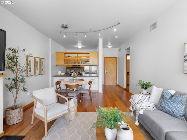 living area with rail lighting, visible vents, baseboards, and light wood-style floors