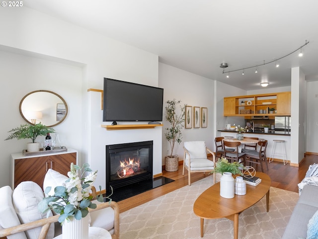 living room with a fireplace with flush hearth, rail lighting, and light wood-type flooring