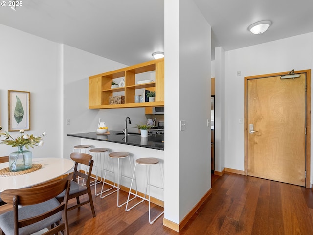 kitchen featuring a sink, stainless steel microwave, a breakfast bar, and dark wood finished floors