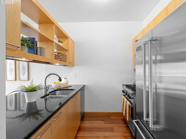 kitchen featuring open shelves, a sink, dark stone counters, wood finished floors, and premium appliances
