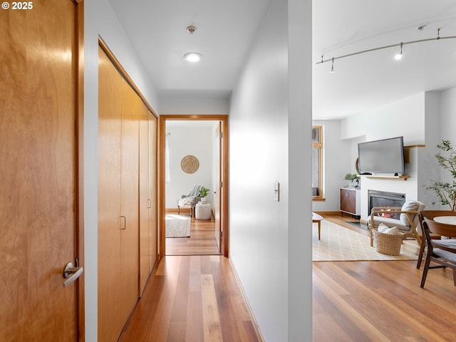 hallway featuring baseboards, rail lighting, and light wood-style flooring