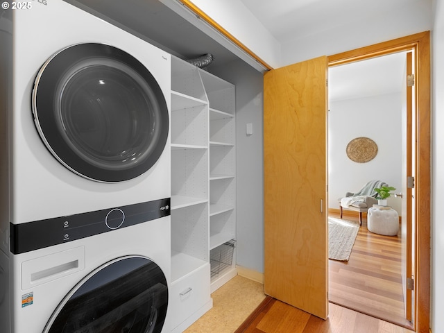 laundry area featuring stacked washer / drying machine, wood finished floors, and laundry area