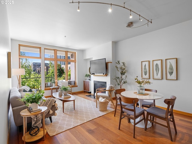 dining space featuring rail lighting, a fireplace with flush hearth, and wood finished floors