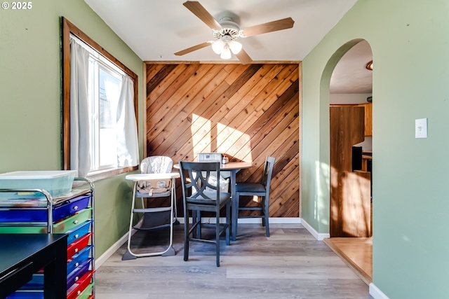 dining space featuring ceiling fan, wooden walls, and light hardwood / wood-style flooring