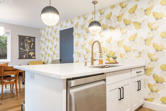 kitchen featuring dishwasher, a sink, light countertops, wallpapered walls, and light wood-style flooring