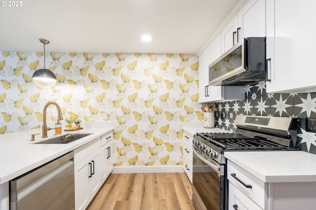 kitchen featuring wallpapered walls, appliances with stainless steel finishes, and a sink