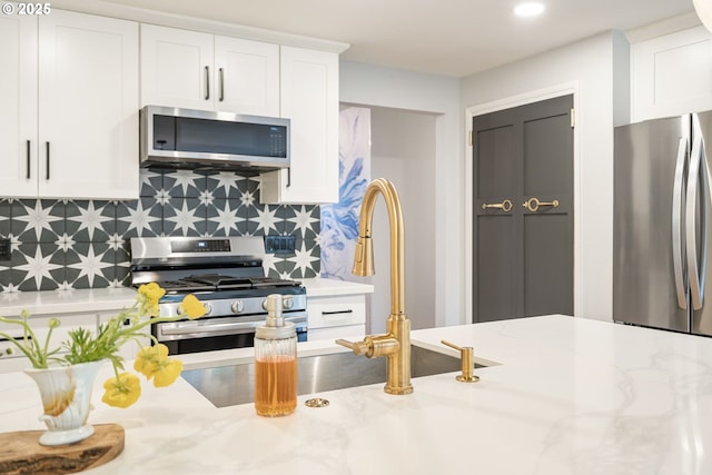 kitchen featuring recessed lighting, white cabinets, light stone counters, appliances with stainless steel finishes, and backsplash