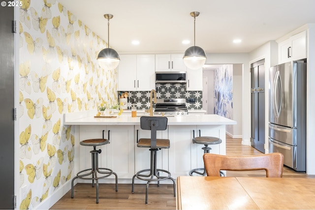 kitchen featuring light countertops, a breakfast bar, stainless steel appliances, and wallpapered walls
