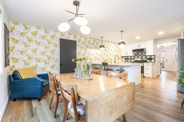 dining area featuring baseboards, an accent wall, light wood-type flooring, and wallpapered walls