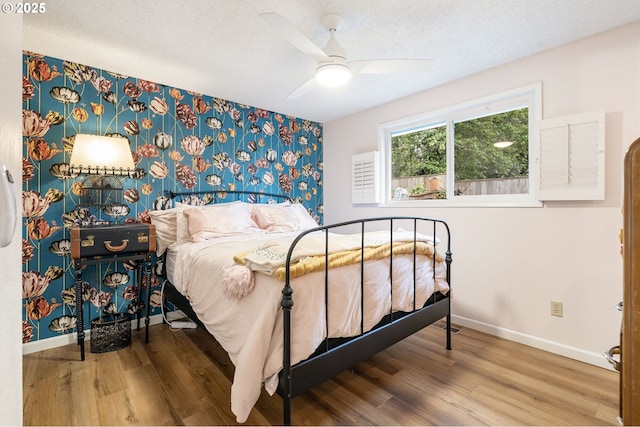 bedroom with baseboards, an accent wall, wallpapered walls, and wood finished floors