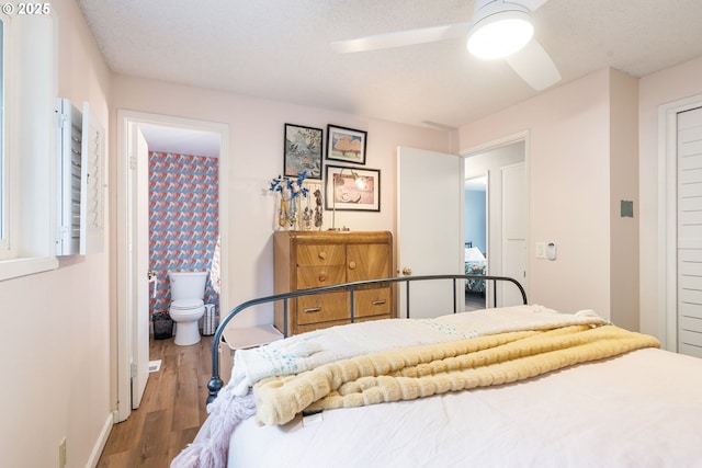 bedroom with baseboards, a ceiling fan, ensuite bath, and wood finished floors