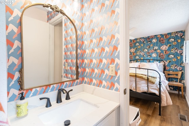 bathroom featuring visible vents, vanity, wood finished floors, wallpapered walls, and a textured ceiling