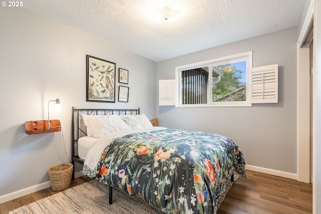 bedroom with a textured ceiling, baseboards, and wood finished floors
