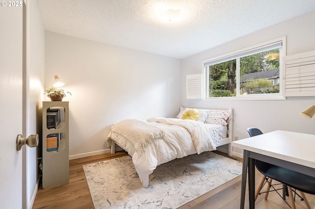 bedroom featuring baseboards, a textured ceiling, and wood finished floors