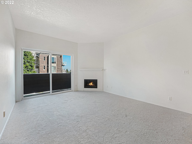 4320 S Corbett Ave Unit 206, Portland, OR 97239 - unfurnished living room featuring carpet floors, a textured ceiling, a lit fireplace, and baseboards