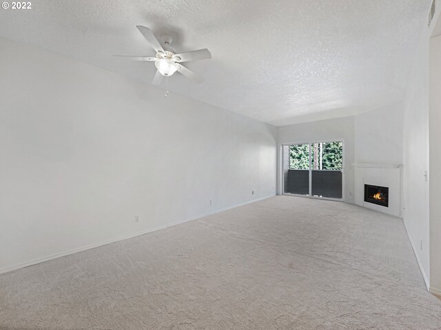 4320 S Corbett Ave Unit 206, Portland, OR 97239 - unfurnished living room with a textured ceiling, baseboards, a lit fireplace, a ceiling fan, and carpet